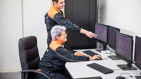 Senior female Mondi worker sits at a computer while a younger male colleague points to data on the screen.